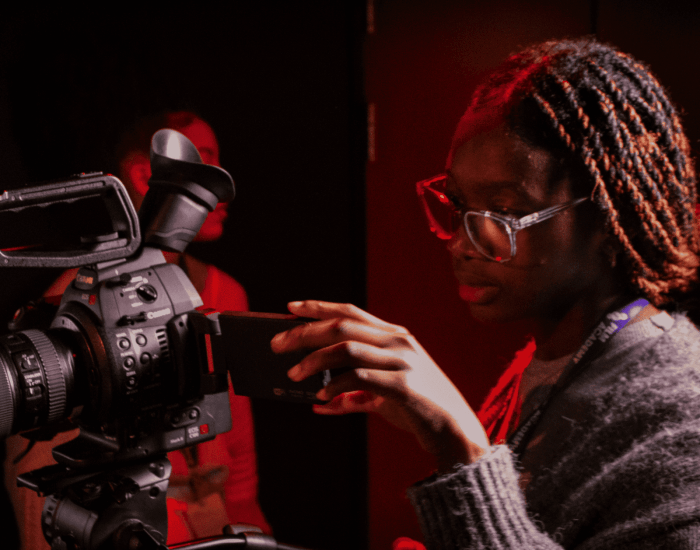 A BFI Film Academy short course student sets up a shot in a darkened room with red back lighting
