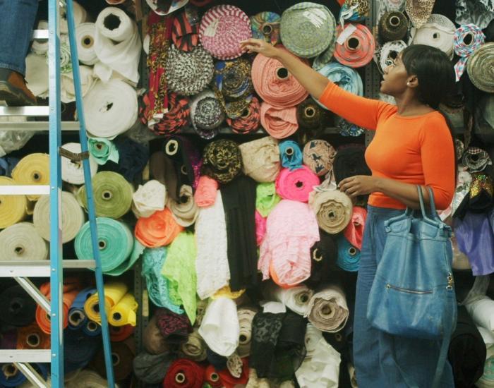 A young woman chooses fabrics at a fabric shop, directing a man up a ladder