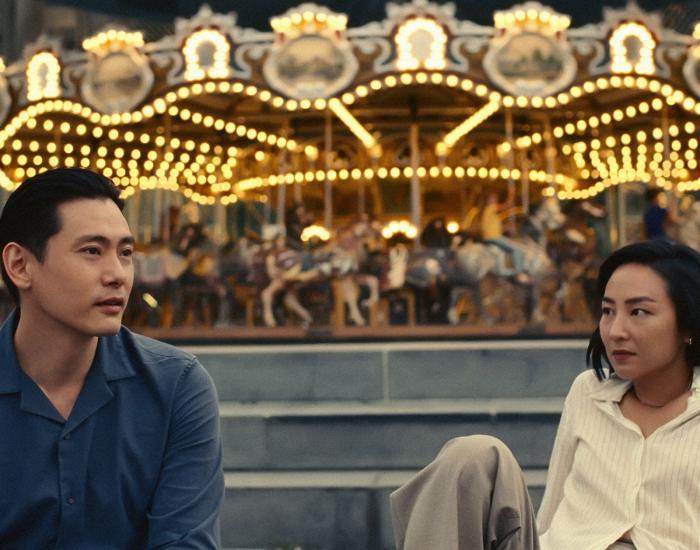 A young man and woman sit in front of a carousel