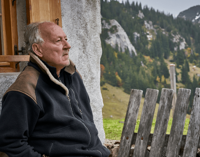 Image of Werner Herzog sitting and looking out at a mountainous landscape