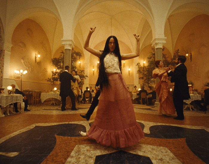 A young, dishevelled woman dances with abandon in a formal ballroom setting