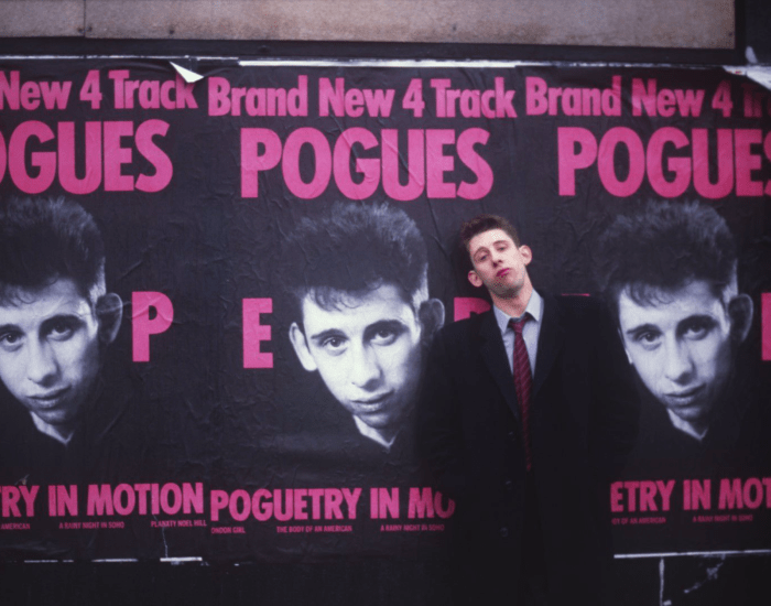 Shane MacGowan stands in front of Pogues posters