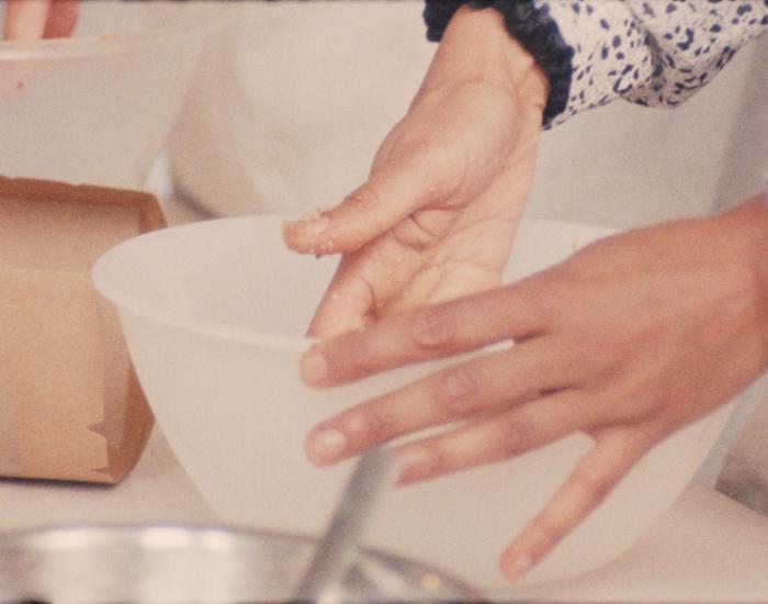 A person's hands in a bowl upon a worktop. They are preparing food.